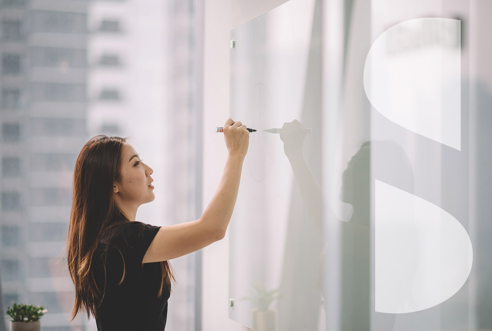 Asian woman writing on a dry-erase board in an office.