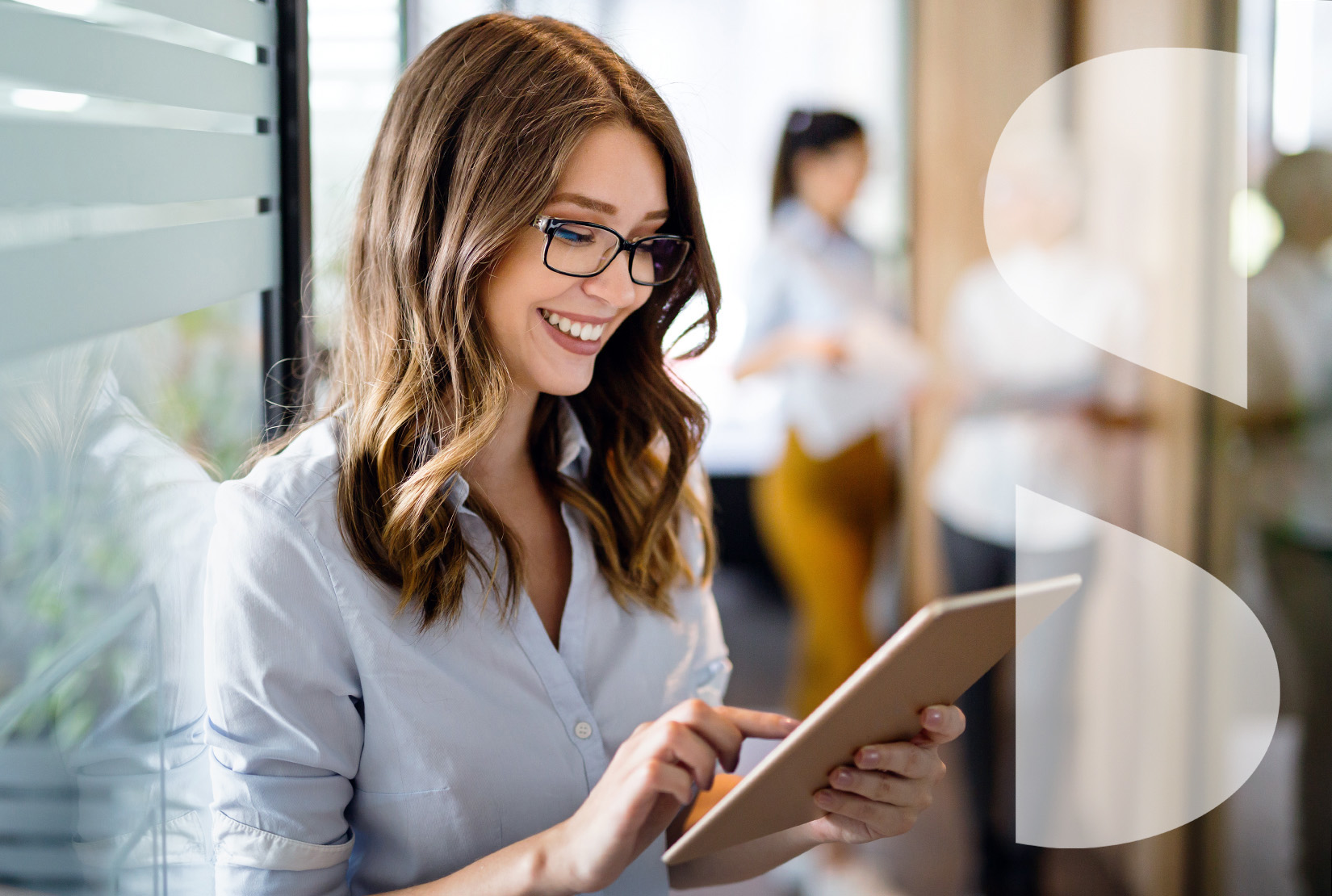 Happy young businesswoman using a digital tablet while standing in front of windows in office