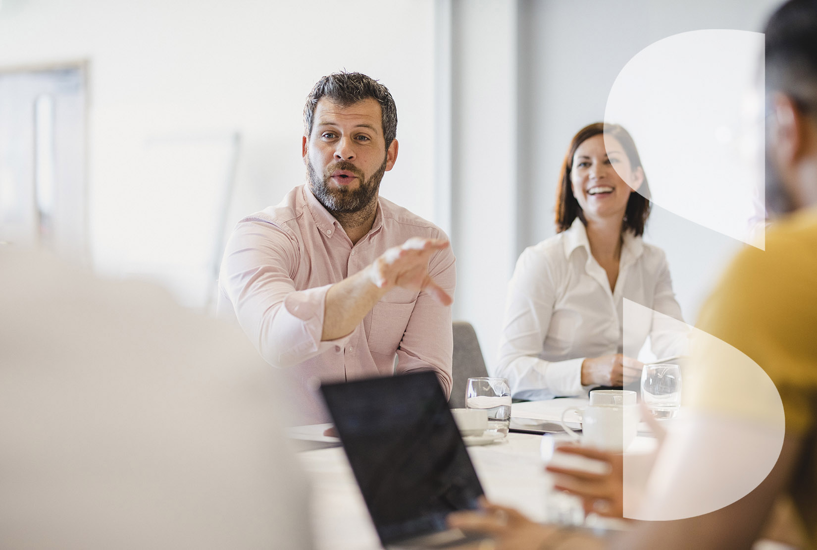 Mature man in his 40s gesturing and talking, sitting at meeting table in board room with coworkers