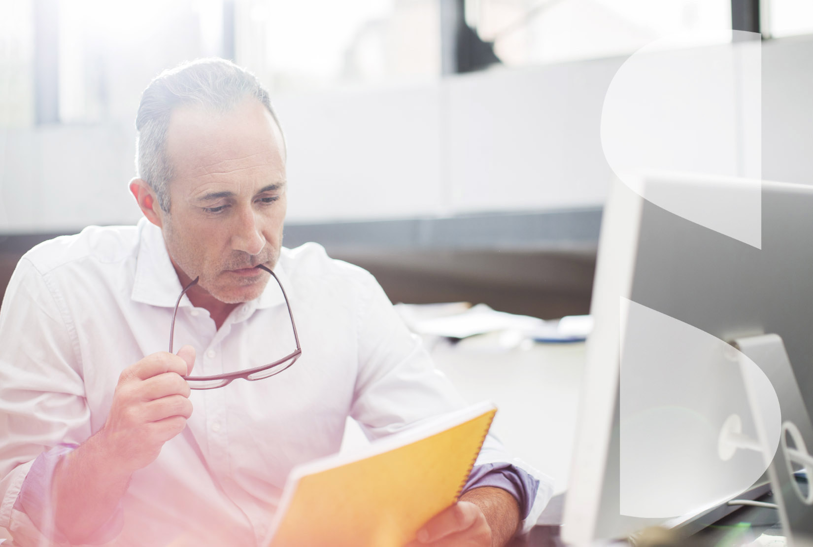 Businessman holding red glasses and reading paperwork at office desk