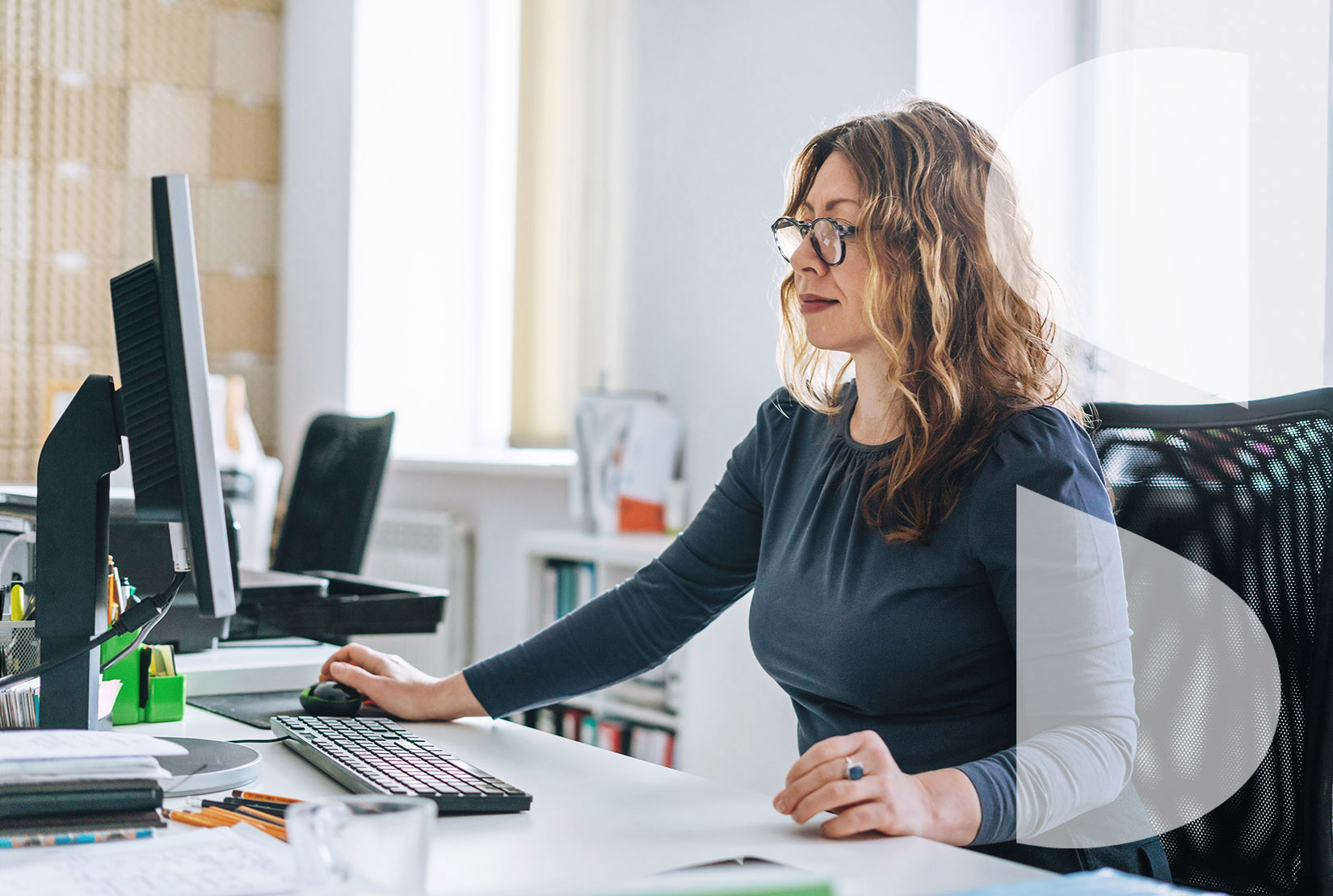 Smiling, adult woman with wavy hair working on computer in bright modern office