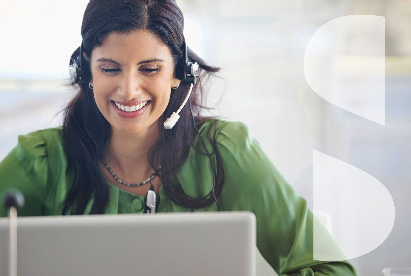 Smiling businesswoman wearing headset while staring at laptop screen