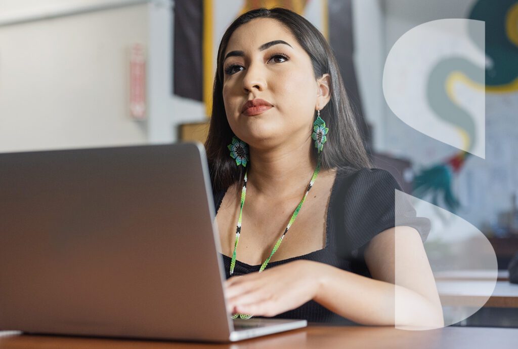 A young Native woman sits behind a laptop at a desk.