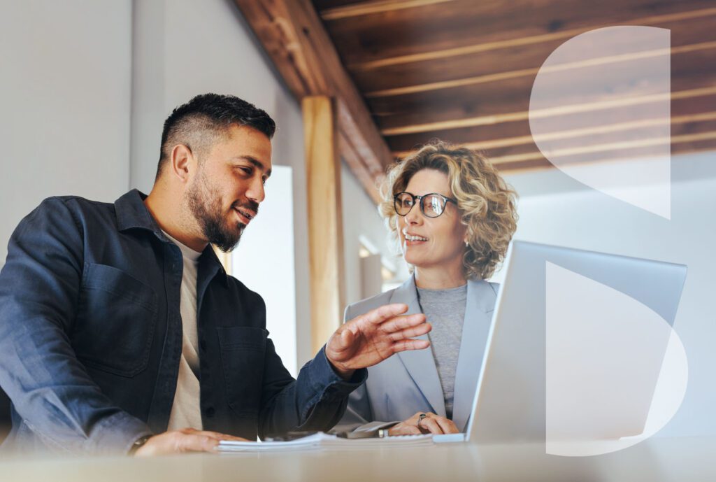 A young man of color and a mature woman look have an engaged conversation at a laptop.