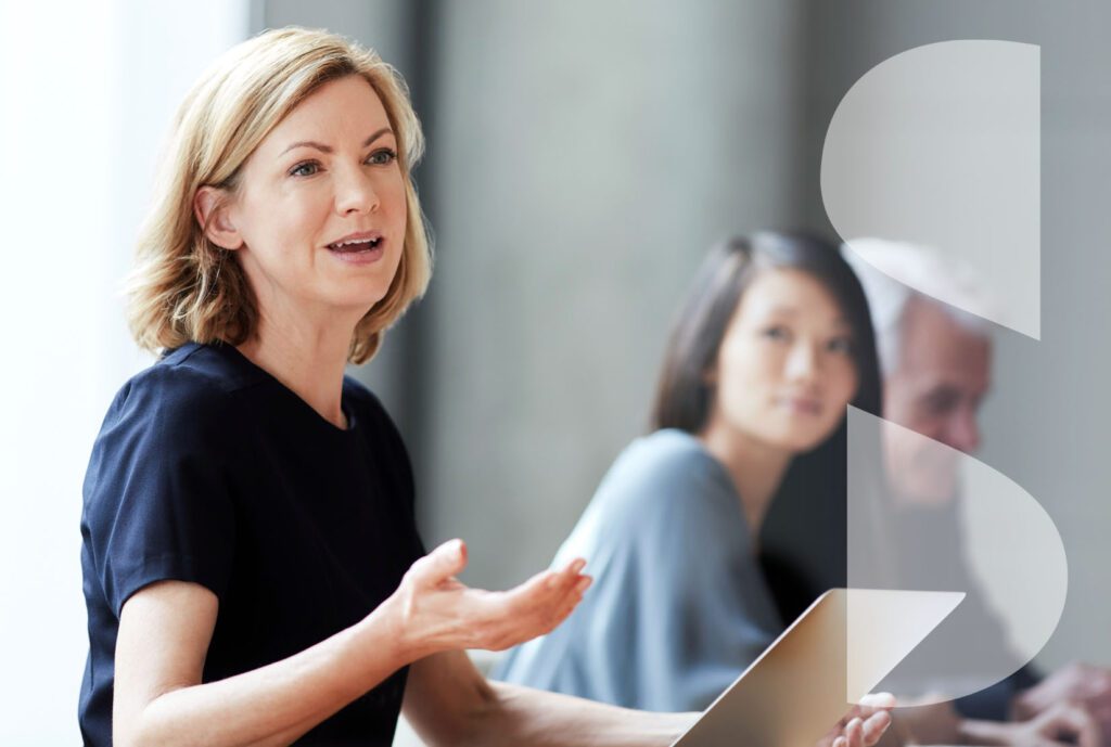 A confident middle-aged female executive with a laptop leads a meeting.